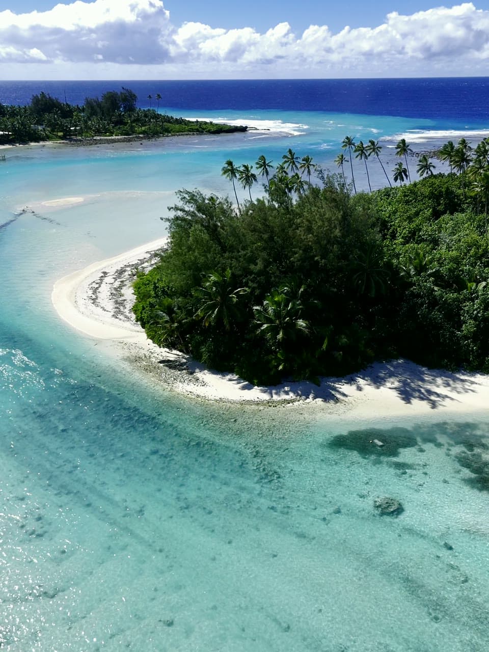 Aerial view of a turquoise Cook Islands lagoon and palm-covered islet